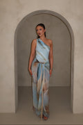 Woman in a one-shoulder blue swimsuit standing in an archway with a neutral background